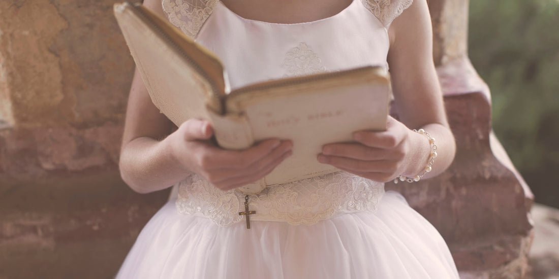 Little girl in her white lace First Communion dress reading an heirloom Bible wearing pearl jewelry.